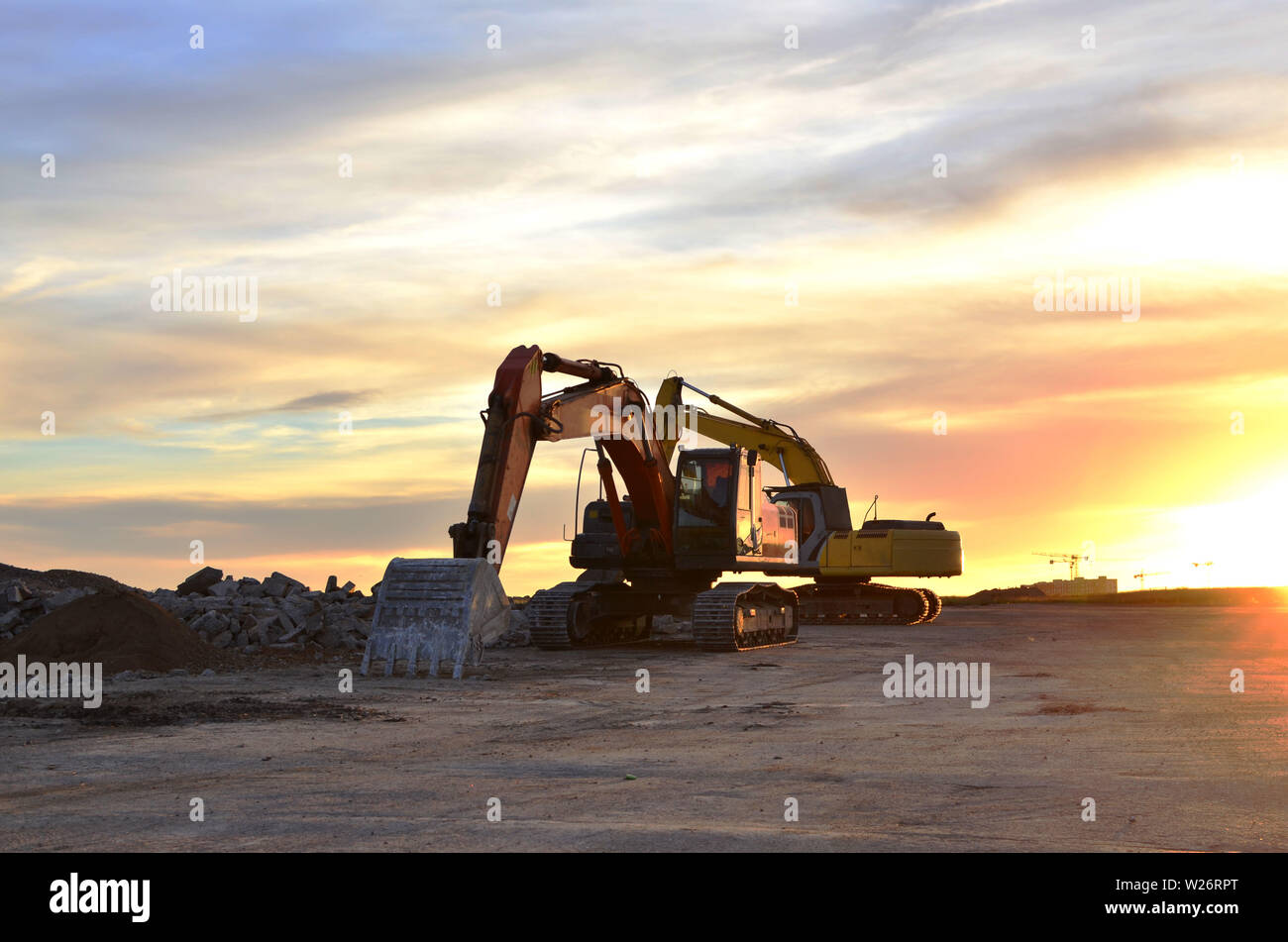 Heavy tracked excavators at a construction site on a background sunset