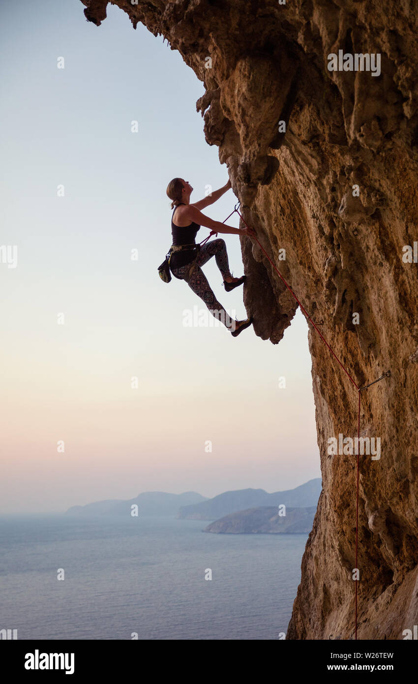 Caucasian young woman climbing challenging route at sunset Stock Photo