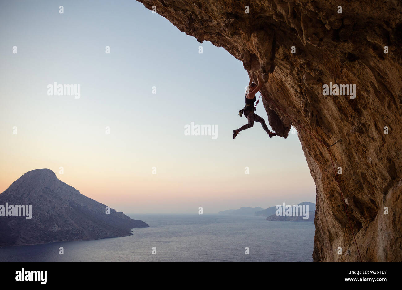 Caucasian young woman climbing challenging route at sunset Stock Photo