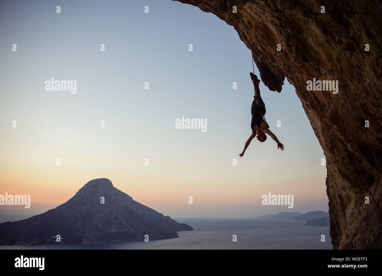 Young female rock climber swinging on rope upside down while being lowered down Stock Photo