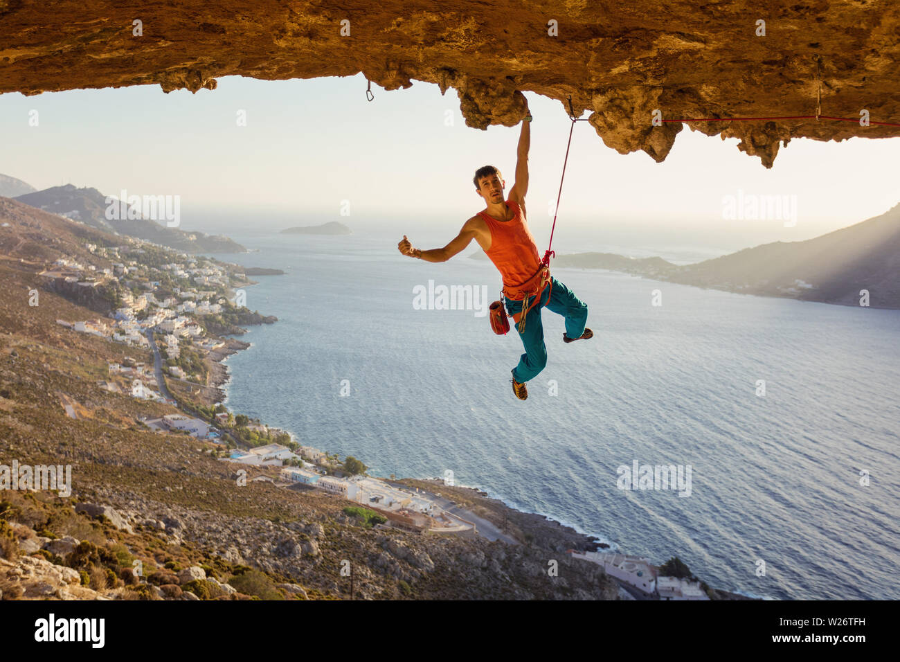 Male rock climber hanging on cliff with one hand and showing thumb up Stock Photo
