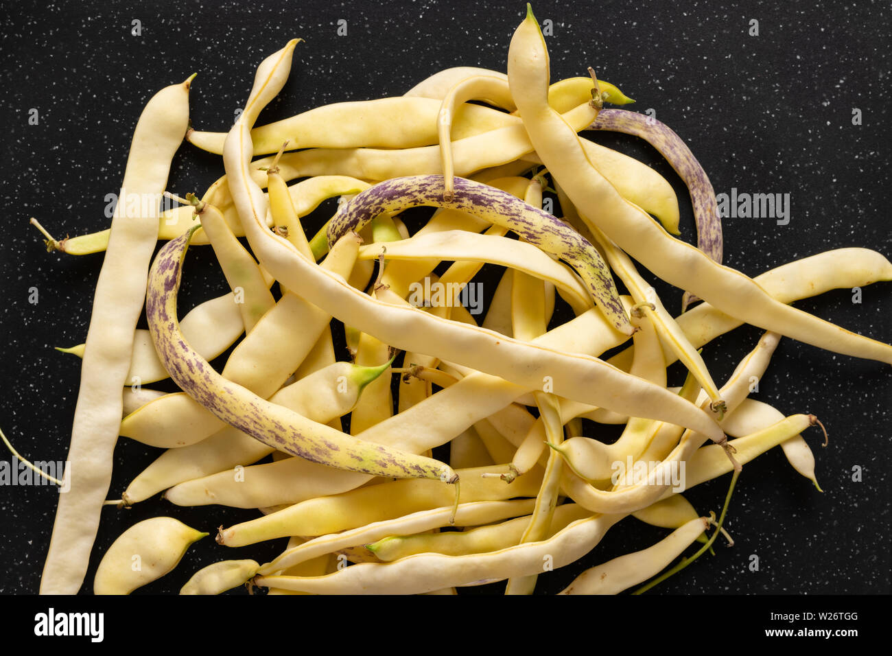Organic flat yellow wax beans pile on black cut board. Stock Photo
