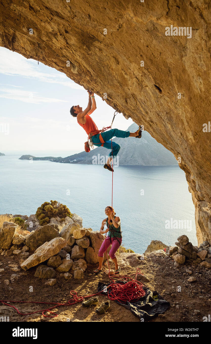 Young man starts climbing challenging route in cave, his female partner