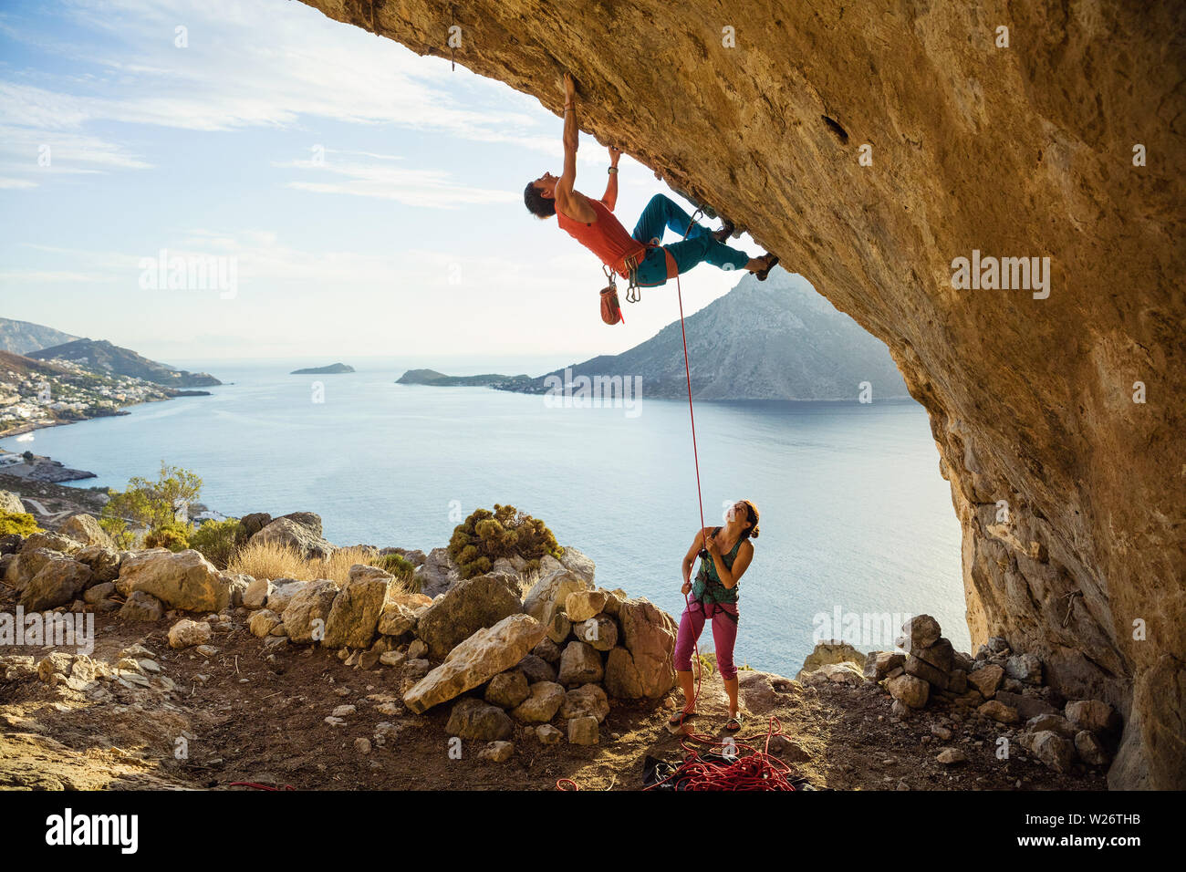 Young man starts climbing challenging route in cave, his female partner