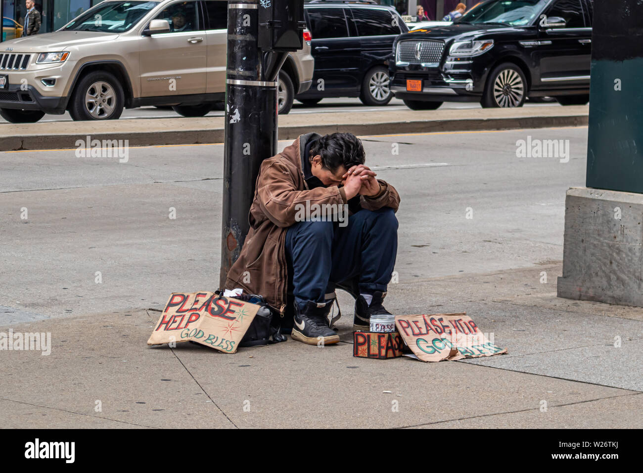 USA, Chicago, Illinois. May 9, 2019. Homeless man sitting on the roadside and cardboard signs asking for help, downtown Stock Photo