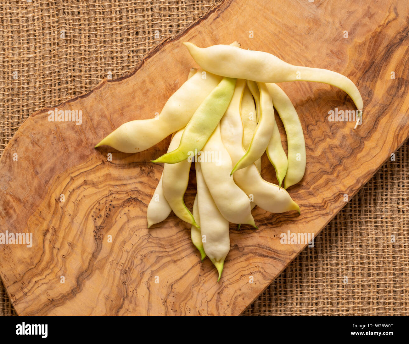 Organic flat yellow wax beans pile on jute fabric and olive wood cut board background Stock