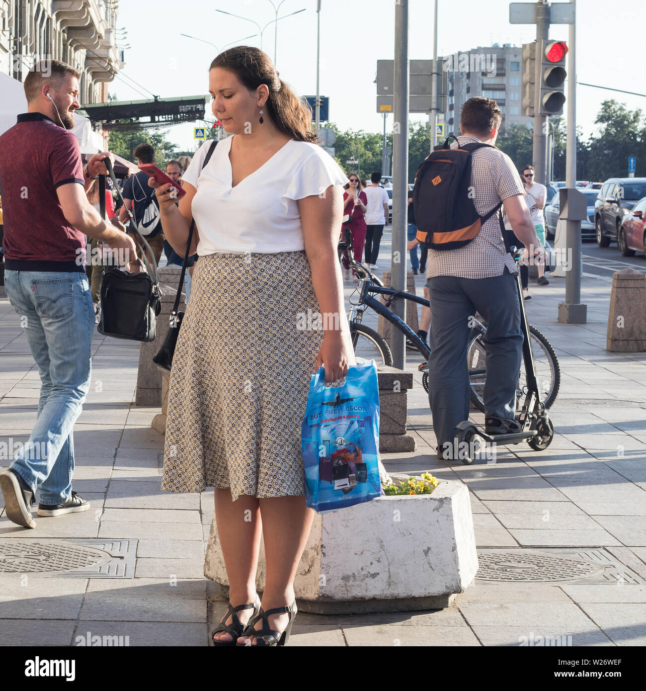 Moscow, RUSSIA - July 2, 2019 girl with long hair in a white blouse and a plaid skirt is waiting for friends Stock Photo
