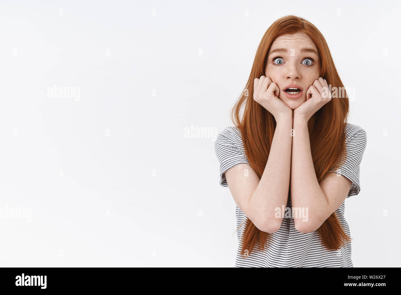 Shocked panicking freaked out young worried redhead girl popping eyes scared look concerned hold hands jawline trembling screaming horrified, watching Stock Photo