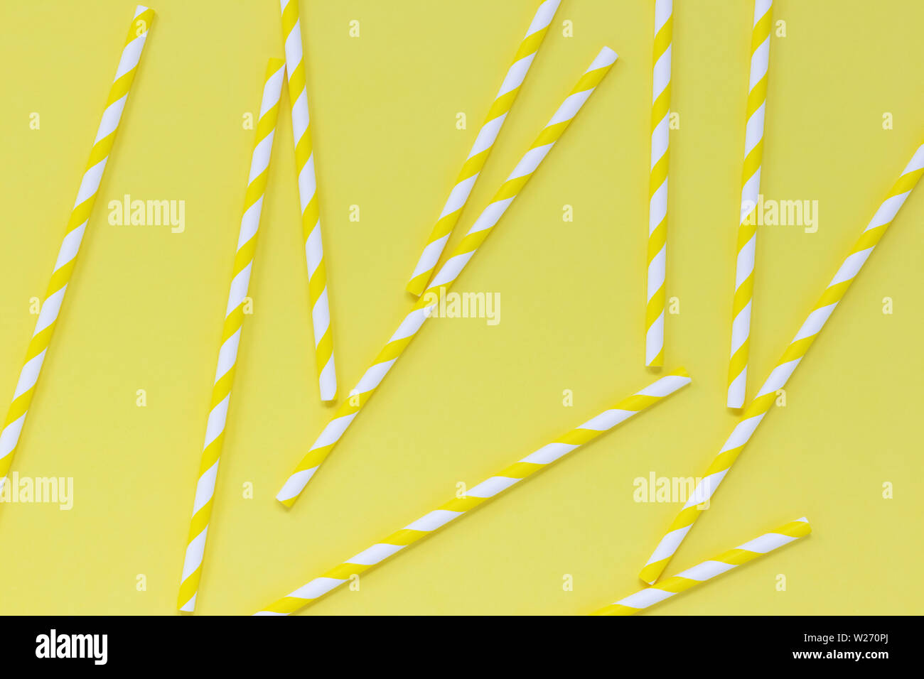 Striped paper straws scattered on a yellow background. Bright summery flat lay. Stock Photo