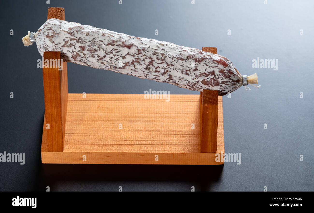 Whole spicy cured Italian salami displayed on a wooden stand over a dark grey background with