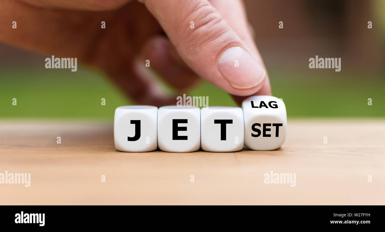 Hand turns a dice and changes the word 'jet-set' to 'jet-lag'. Stock Photo