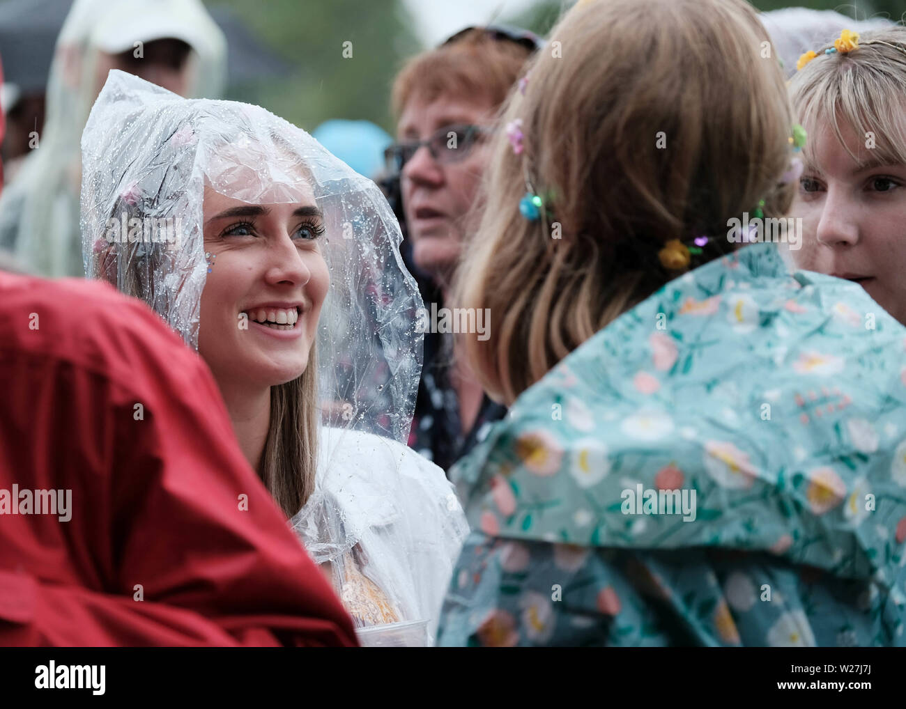 Great Tew, Oxfordshire, UK. , July 6th 2019. Women in crowd wearing rain ponchos smiling at Cornbury Festival, Great Tew, Oxfordshire, UK.  Credit: Dawn Fletcher-Park/Alamy Live News Stock Photo