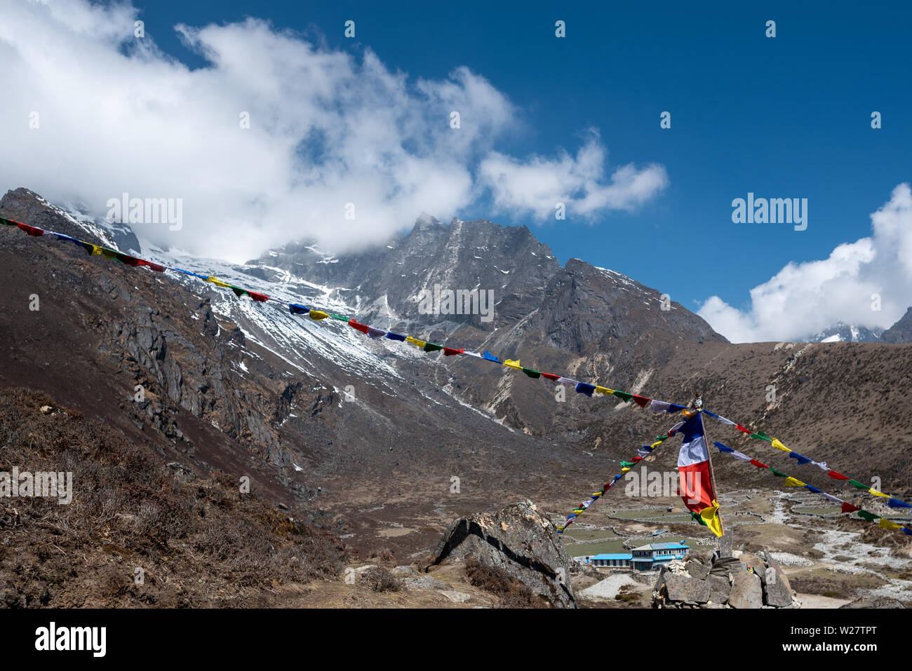 Traditional buddhist flags with mantras over tiny settlement amidst mountains in Nepal Himalayas Stock Photo