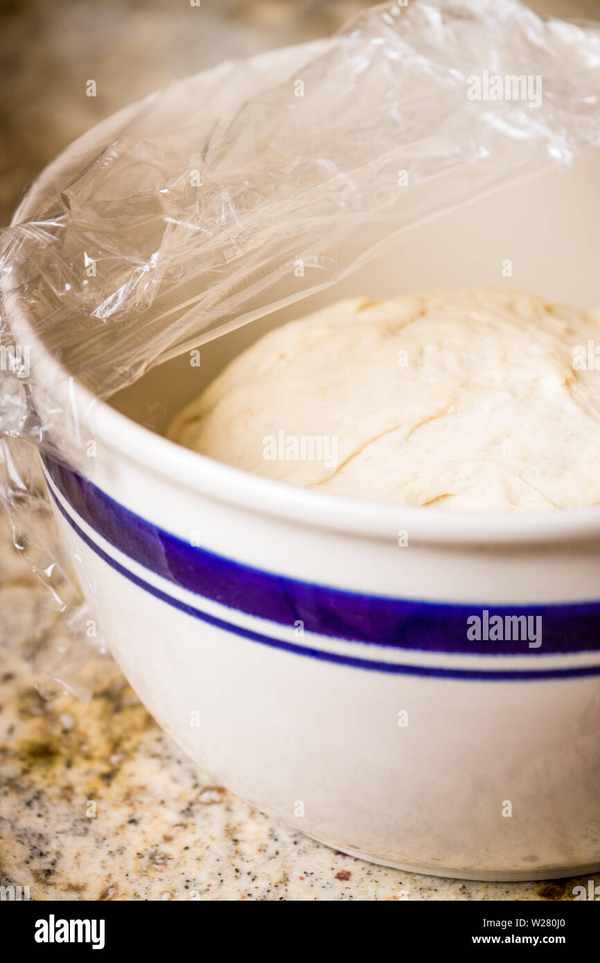 Homemade pizza dough rising in a mixing bowl covered with plastic wrap until doubled in size Stock Photo