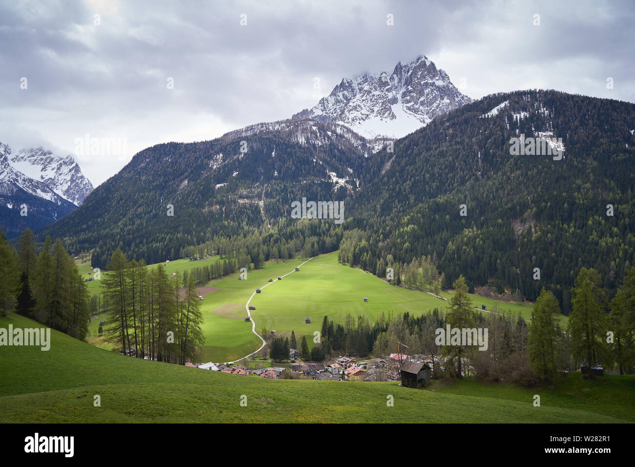 View of a valley in the Alps in the region Trentino with the typical wooden barns (Tabia in Italian) and the Dolomites on the background. Stock Photo