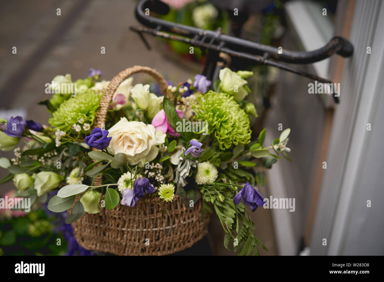 Detail of a parked vintage black bicycle with a bunch of fresh flowers in the front wooden basket. Landscape format. Stock Photo
