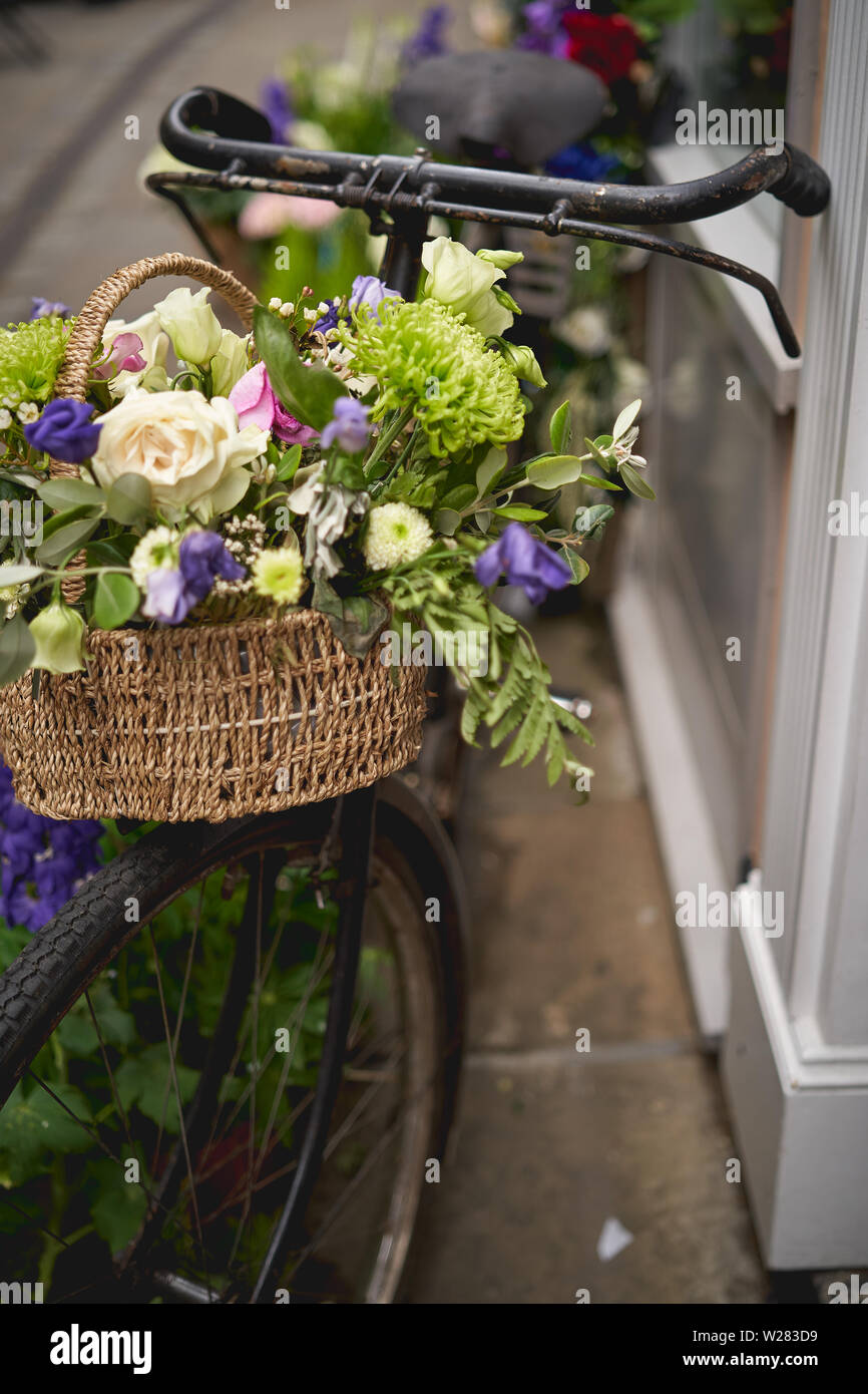 Detail of a parked vintage black bicycle with a bunch of fresh flowers in the front wooden basket. Portrait format. Stock Photo
