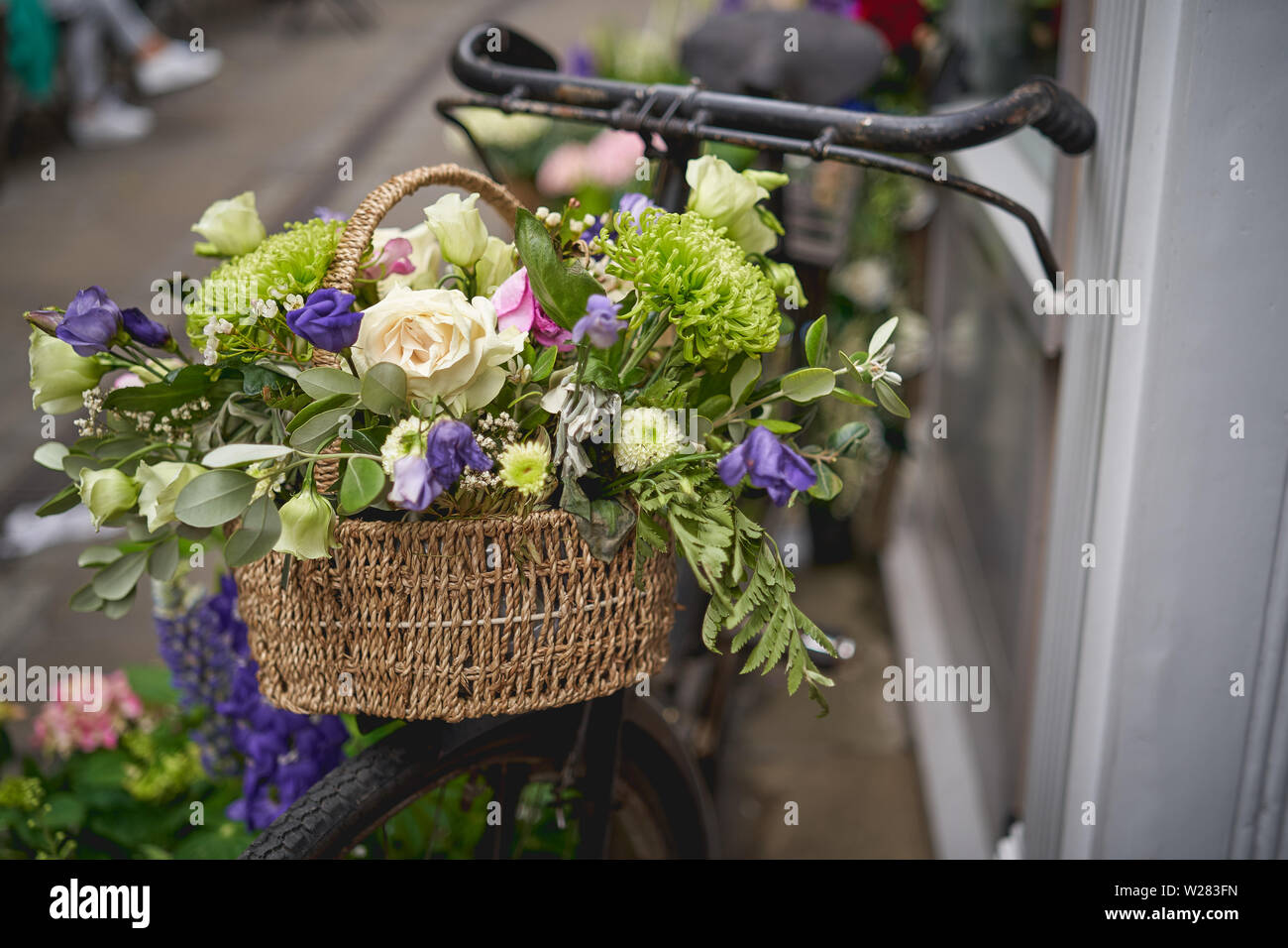 Detail of a parked vintage black bicycle with a bunch of fresh flowers in the front wooden basket. Landscape format. Stock Photo
