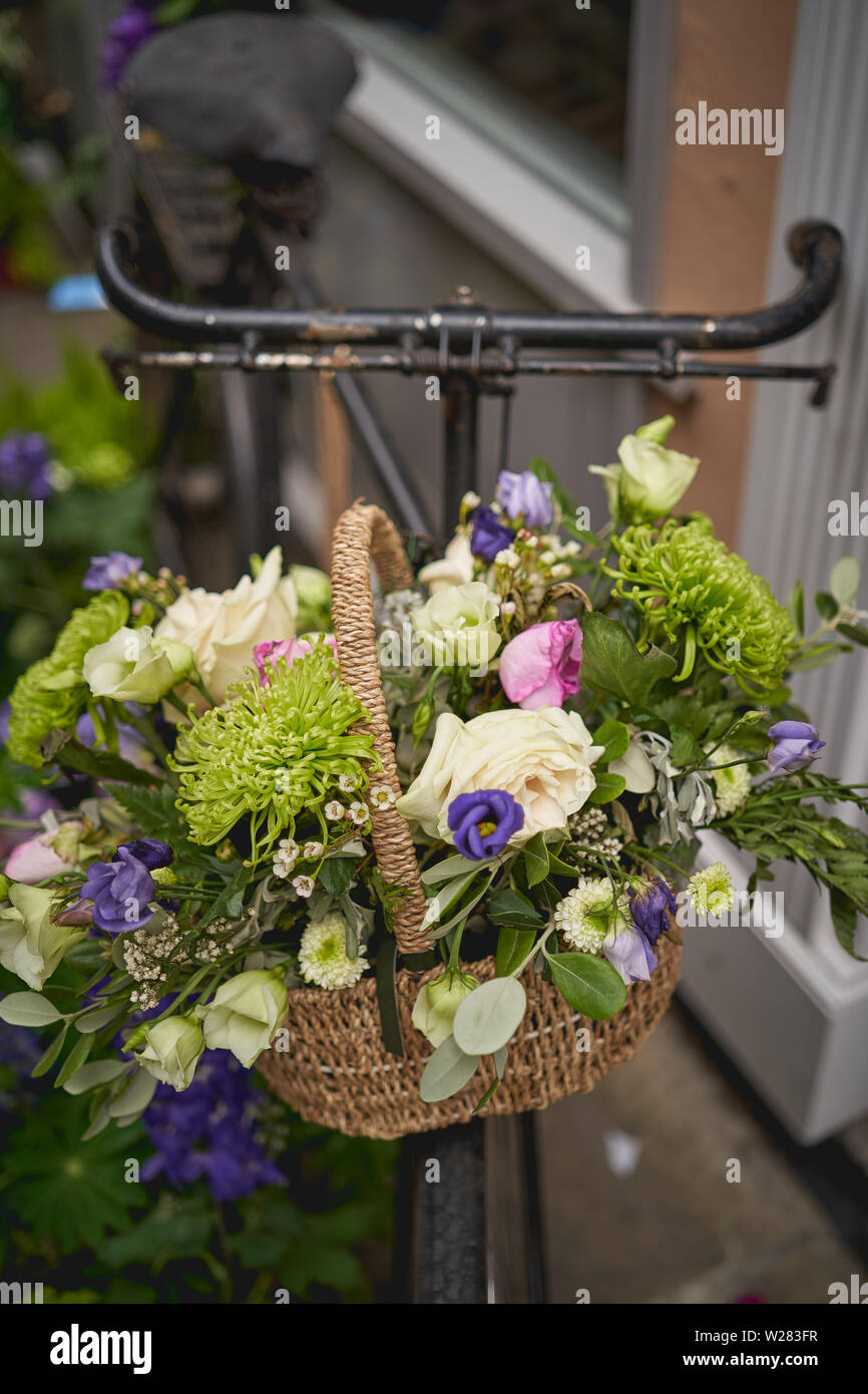 Detail of a parked vintage black bicycle with a bunch of fresh flowers in the front wooden basket. Portrait format. Stock Photo