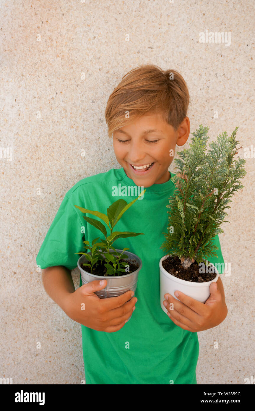 Blond child wearing green t-shirt holding two pots with young plants Stock Photo