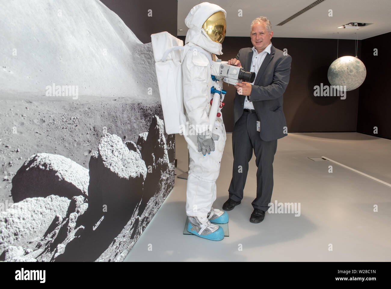 Oberkochen, Germany. 01st July, 2019. Vladan Blahnik, head of lens development, stands next to a space suit in the Zeiss Museum, which is fitted with a Hasselblad medium-format camera with a Zeiss lens. The Swabian company developed special lenses for the NASA Moonlight Program, with which, among other things, the first photos were taken on the moon in July 1969. (to dpa: 'Lenses for the moon' - lenses of the Apollo flights came from Swabia') Credit: Stefan Puchner/dpa/Alamy Live News Stock Photo