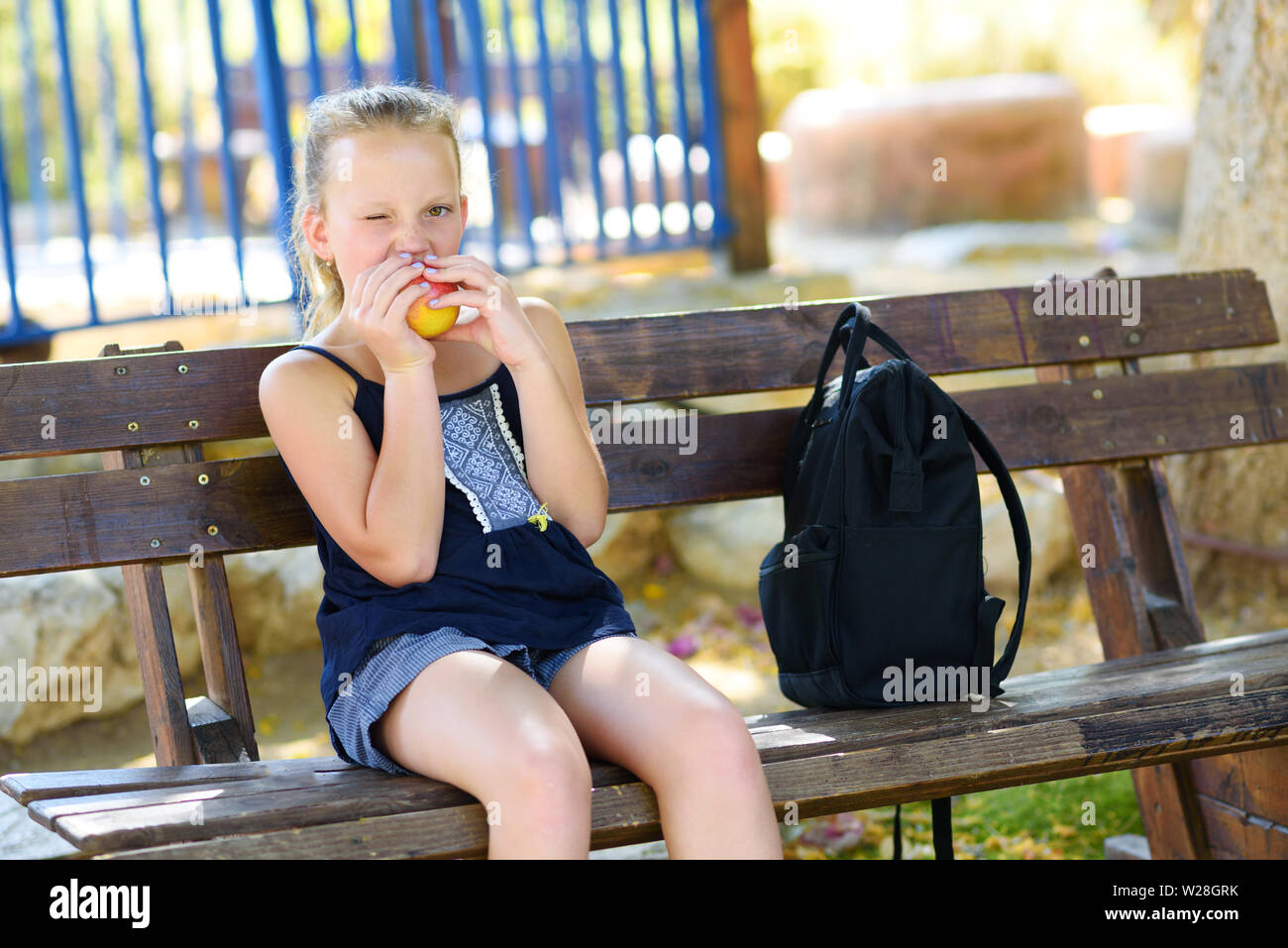 Little girl is eating an apple. Healthy nutrition. Pretty child eating an apple at park , nature outdoors. Teenager pupil enjoying healthy lunch in schoolyard. Stock Photo