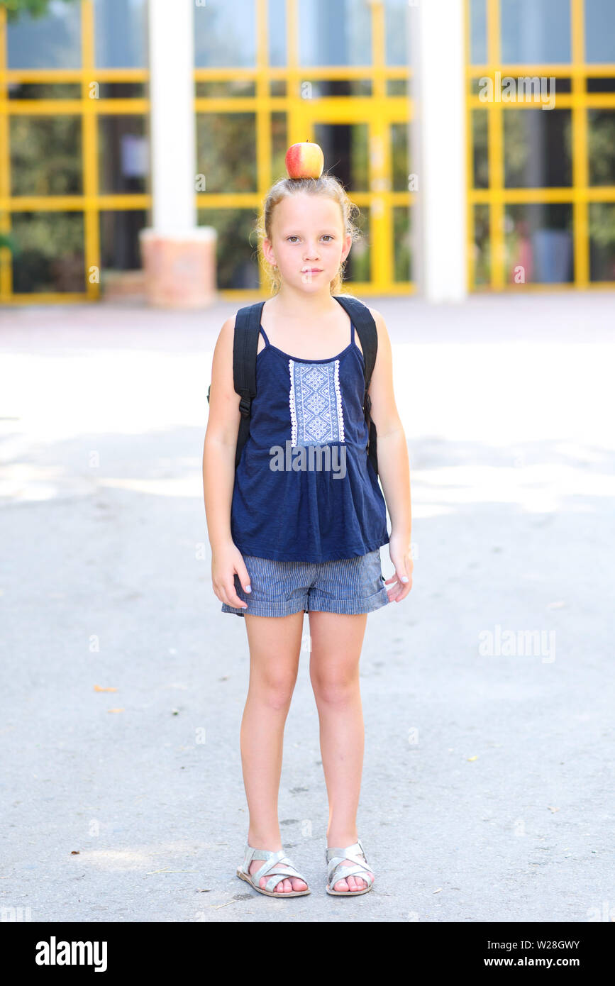 Happy Girl with apple on her head. Great Portrait Of School Pupil Outside Classroom Carrying Bag. Back to school, balance,success,target and healthy eating for child concept. Stock Photo