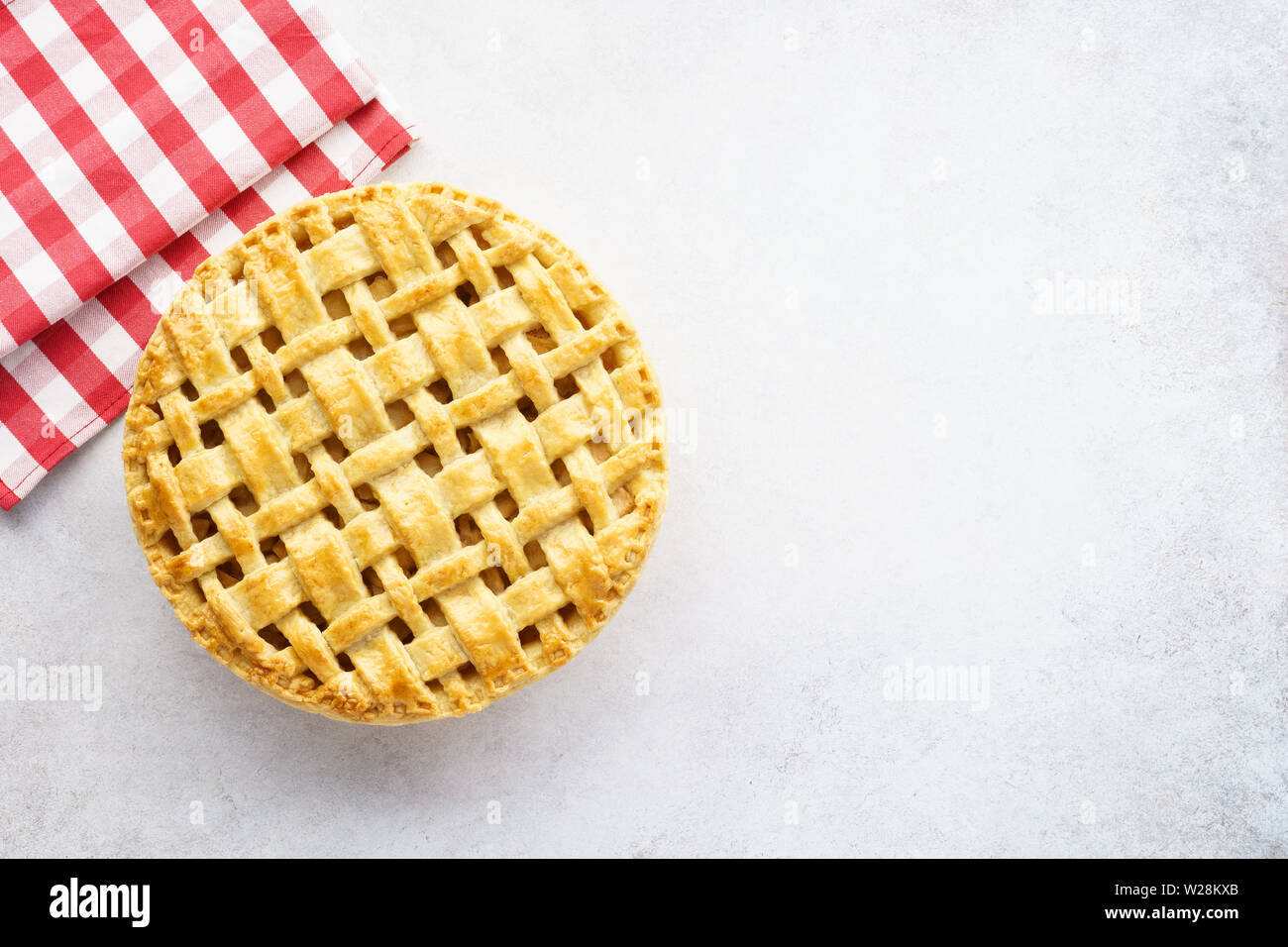 Baked apple pie and red checkered tablecloth on light gray background. Blank space for text. Stock Photo