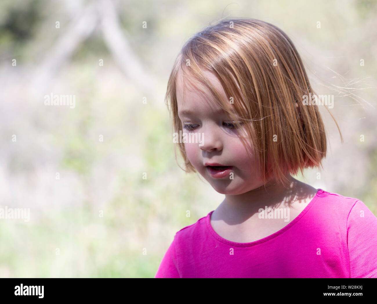 Close up of young girl in pink dress playing in the outdoors Stock Photo