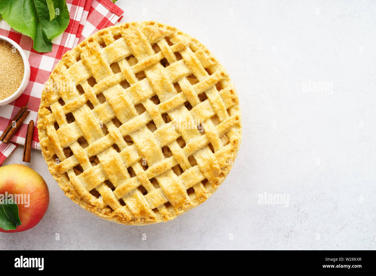 Baked apple pie and ingredients for cooking - sugar, apples, cinnamon. Seasonal pastry background with space for recipe. Stock Photo