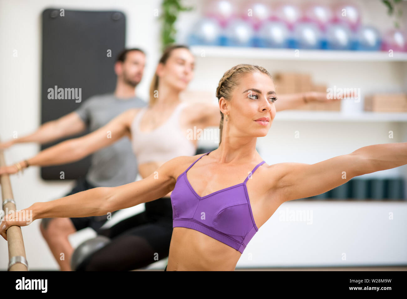 Group of people doing spinal twist exercises using the barre in a gym with focus to a fit athletic toned woman in the foreground in a health and fitne Stock Photo