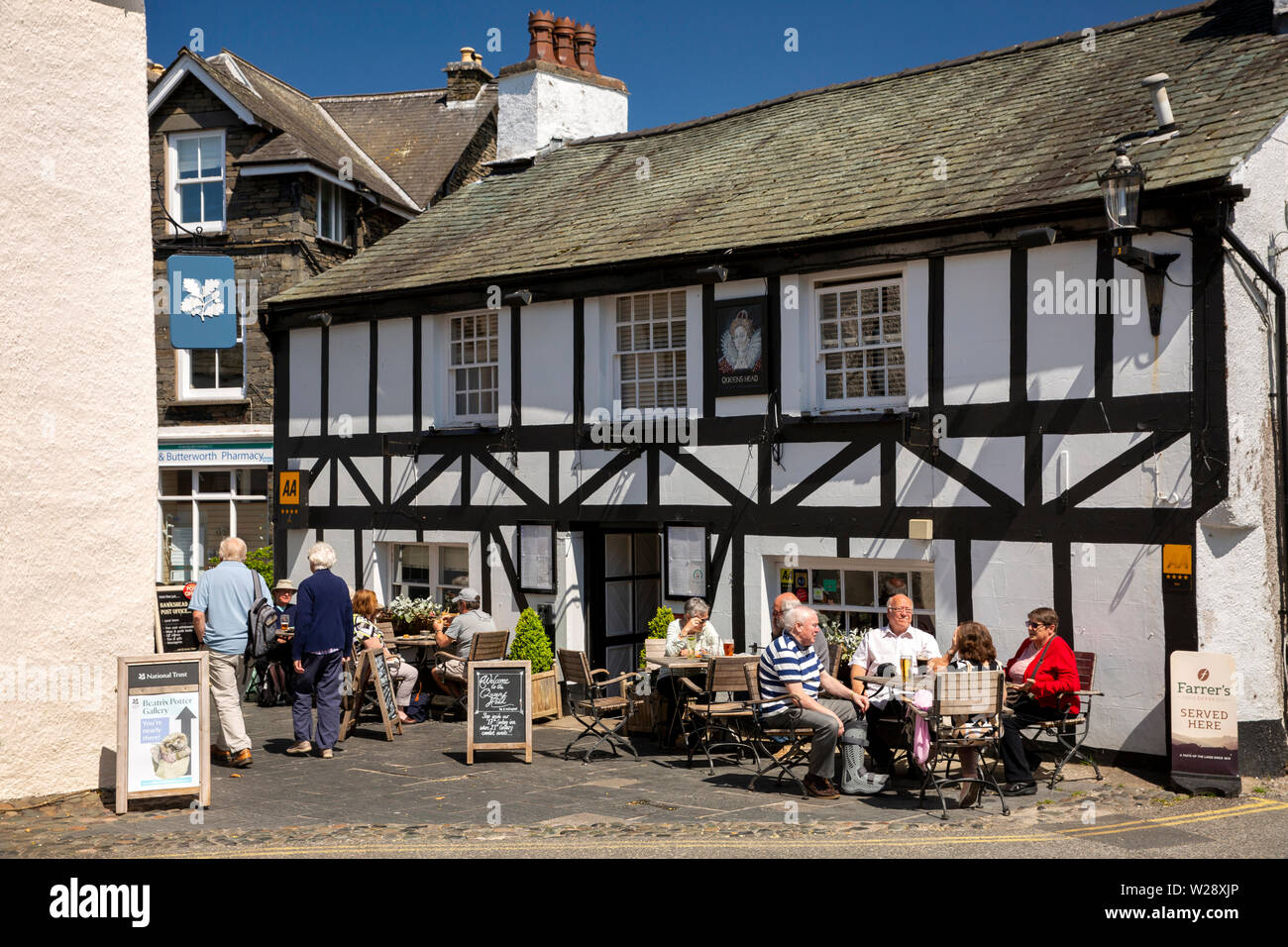 UK, Cumbria, Hawkshead, Main Street, customers sat in sunshine outside Queen’s Head Inn Stock Photo