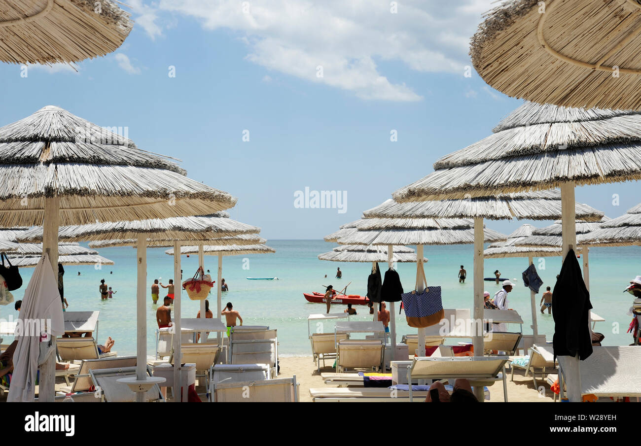 Beautiful beach resort with white straw umbrellas on a blue sky and white clouds. On the background some people having fun on the beach. Clear sea. Be Stock Photo
