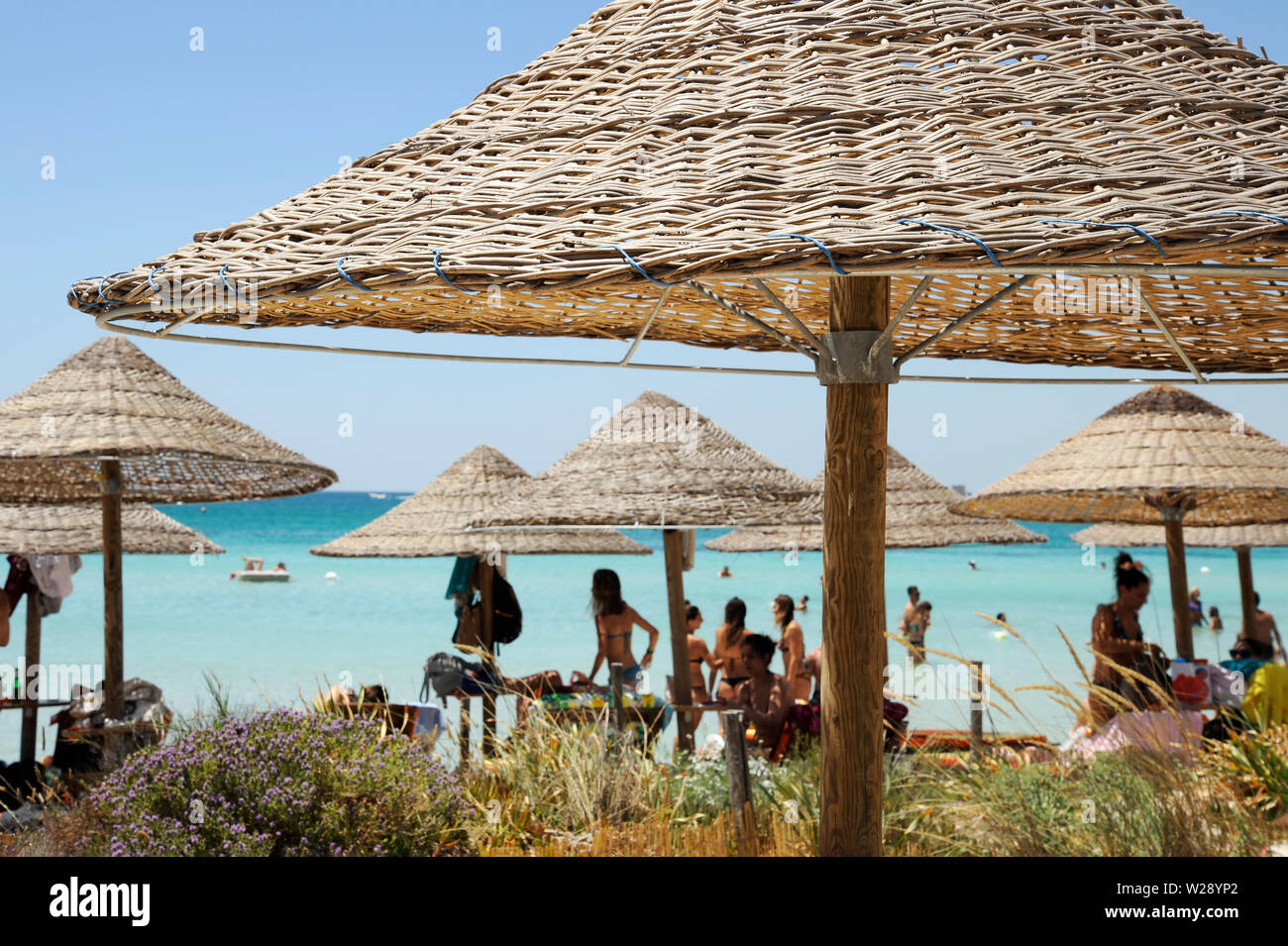 Beautiful beach resort with straw umbrellas on a blue sky and white clouds. On the background some people having fun on the beach. Clear sea. Beach li Stock Photo