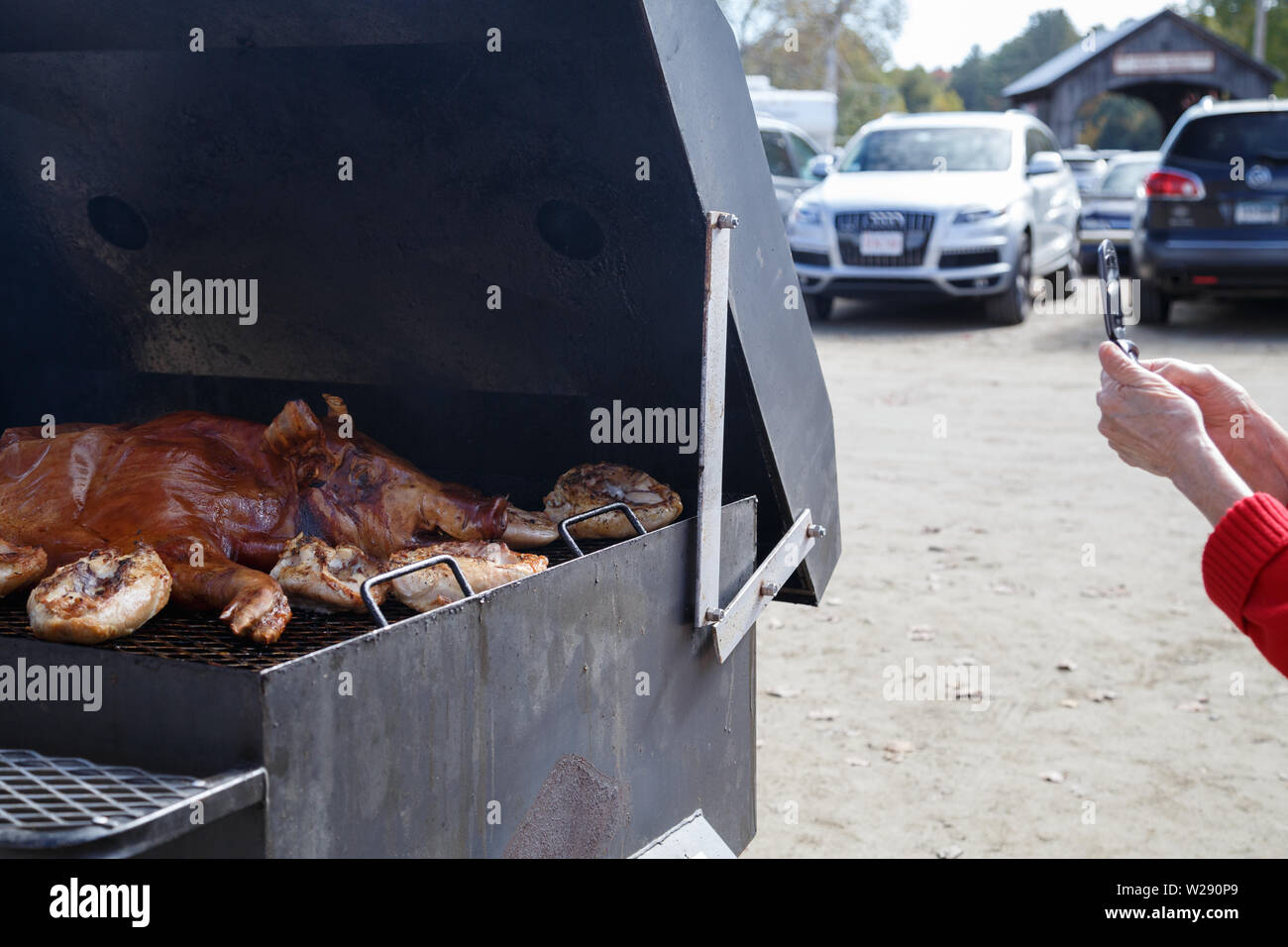 A visitor takes a photo of a pig barbecue held at a parking lot of the Vermont country store in Town of Rockingham, Vermont, USA. Stock Photo