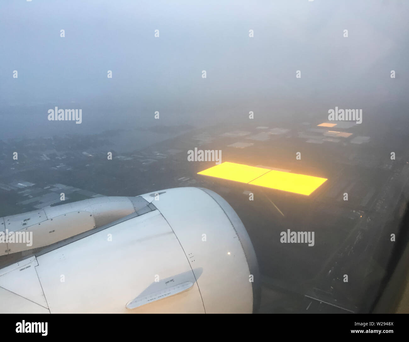 Schiphol, Netherlands - 21 December 2018: Aerial photograph of a large agricultural greenhouses in the Netherlands that are illuminated inside for better growth of the farm products during wintertime. Picture taken from a landing aircraft approaching Amsterdam Schiphol airport at early morning. Stock Photo