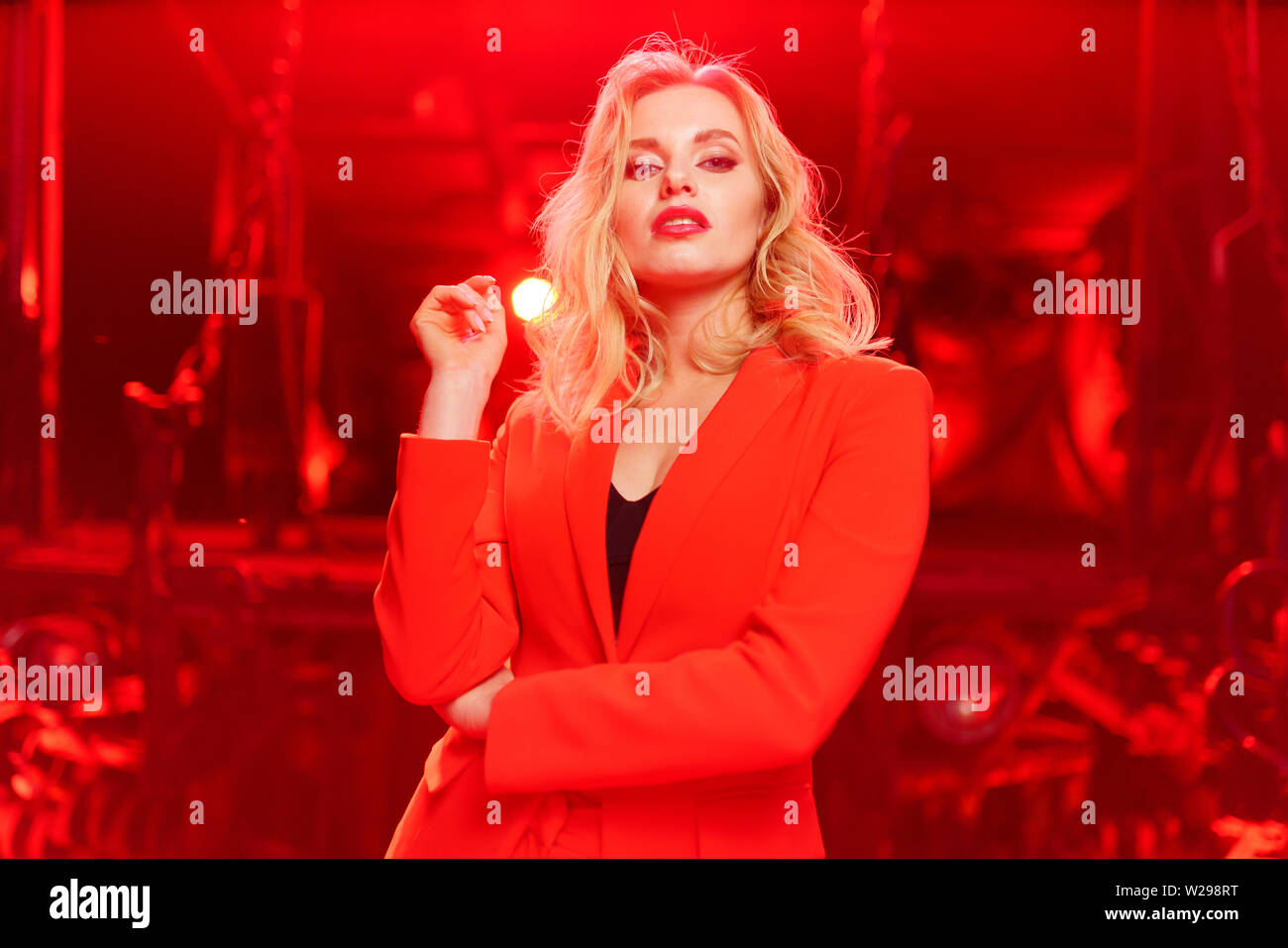 Photo of young blonde woman in red jacket standing on red background Stock Photo