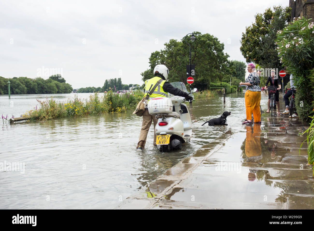 A rider on a scooter pushing his bike through the high water and