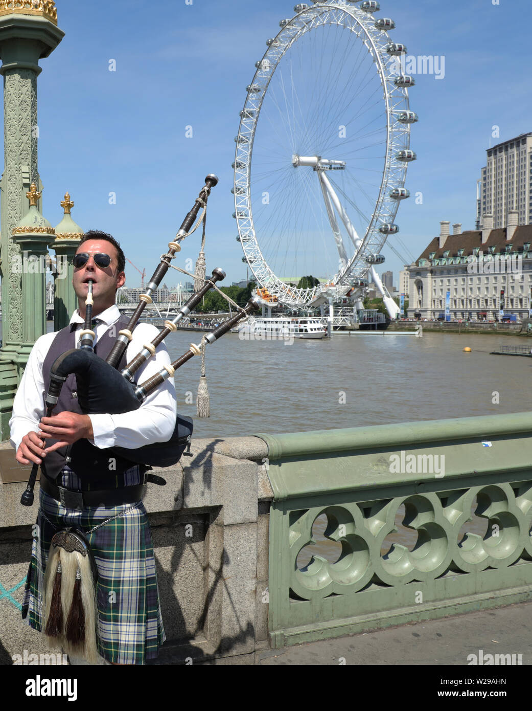 Busker bagpipe player in traditional Scottish outfit plays on