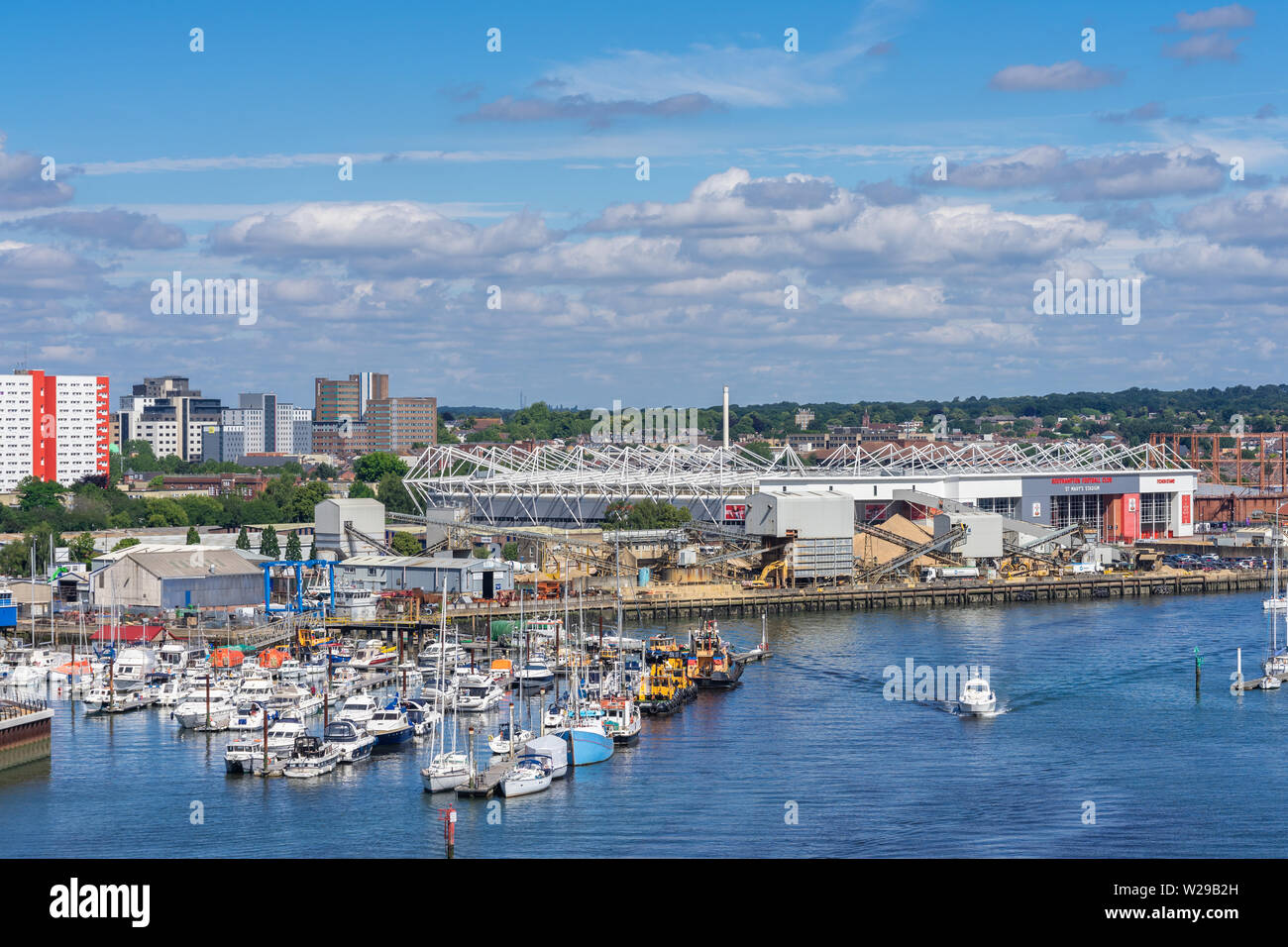 Boats towed along the Itchen river with the St Mary's football stadium in the background, view from Itchen bridge, Southampton, England, UK Stock Photo