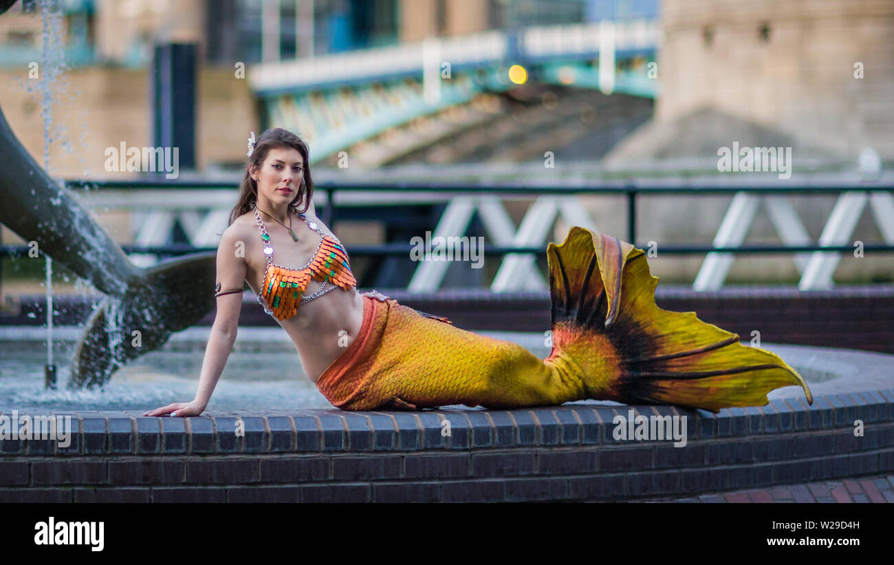 A mermaid poses by the Girl and Dolphin by Tower Bridge in London England. 3 Stock Photo