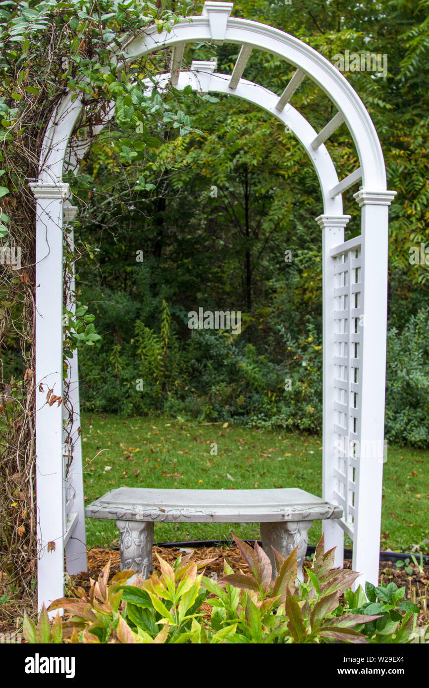 Garden Arbor And Bench In Autumn. White wood garden arch and seat in vertical orientation Stock Photo