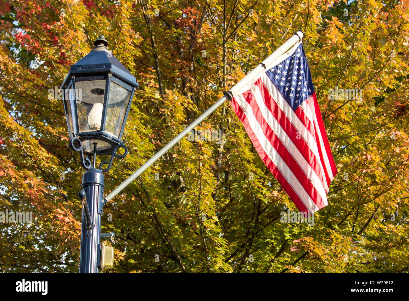 Small Town USA. Main Street lamppost and American flag set against beautiful fall foliage in the Midwest region of America. Stock Photo