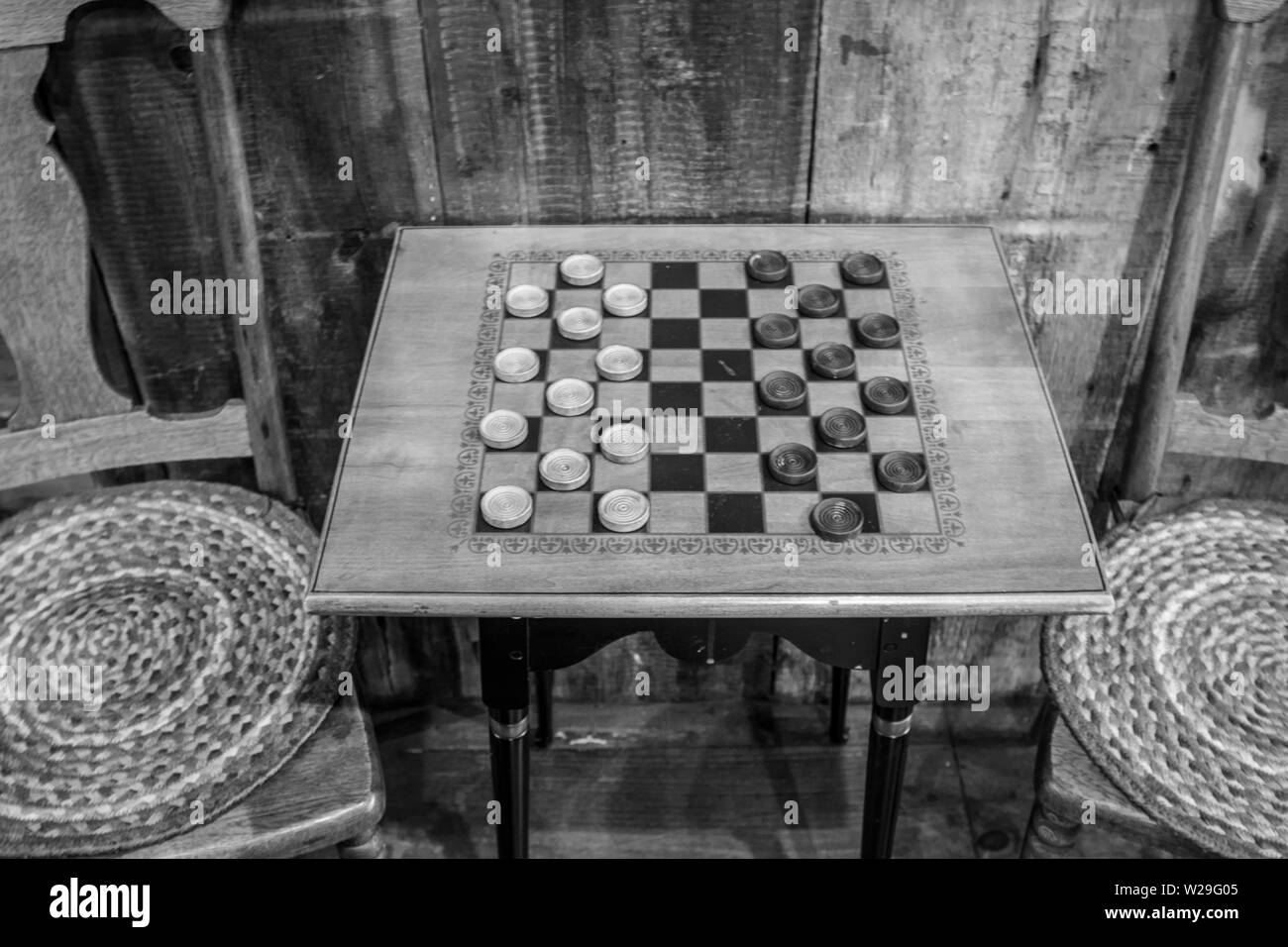 Game Of Checkers. Traditional vintage style wooden checkerboard table with stools in a rural country store. Stock Photo