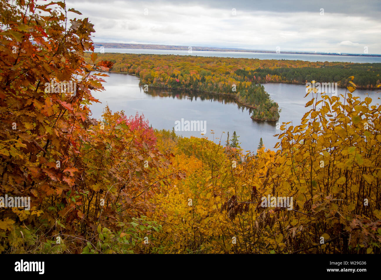 Michigan Autumn Scenic Panorama. Vibrant autumn color in the northern Michigan forest with the vast blue waters of Lake Superior in the background. Stock Photo