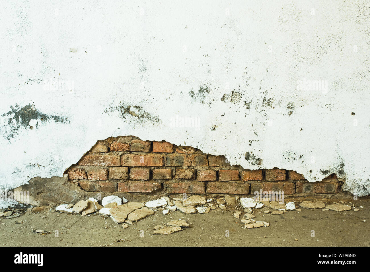 orange bricks peeking out from under a white peeling wall. destroyed