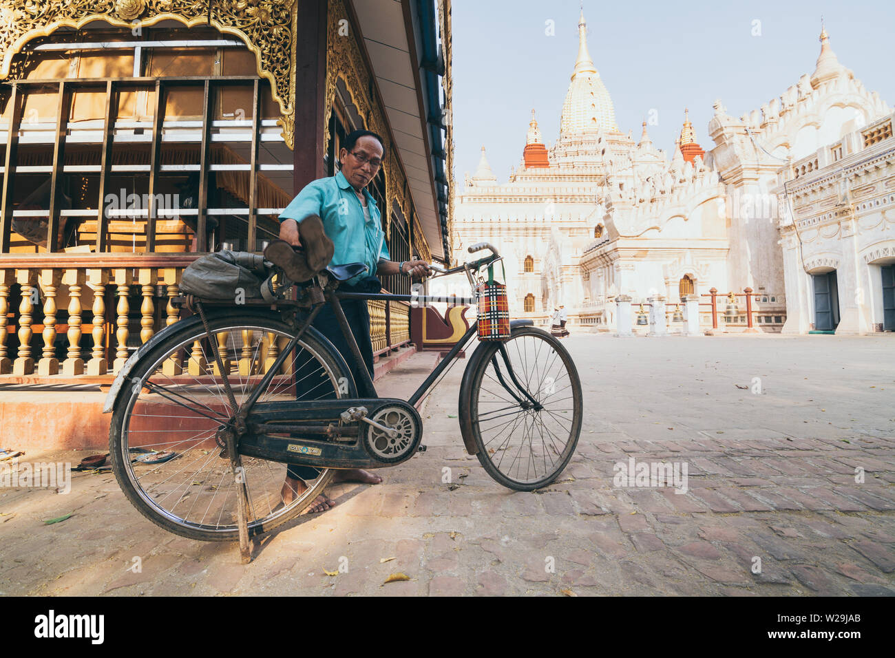 Bagan, Myanmar - March 2019: Burmese man parking bicycle in the backyard of Ananda temple at sunset Stock Photo