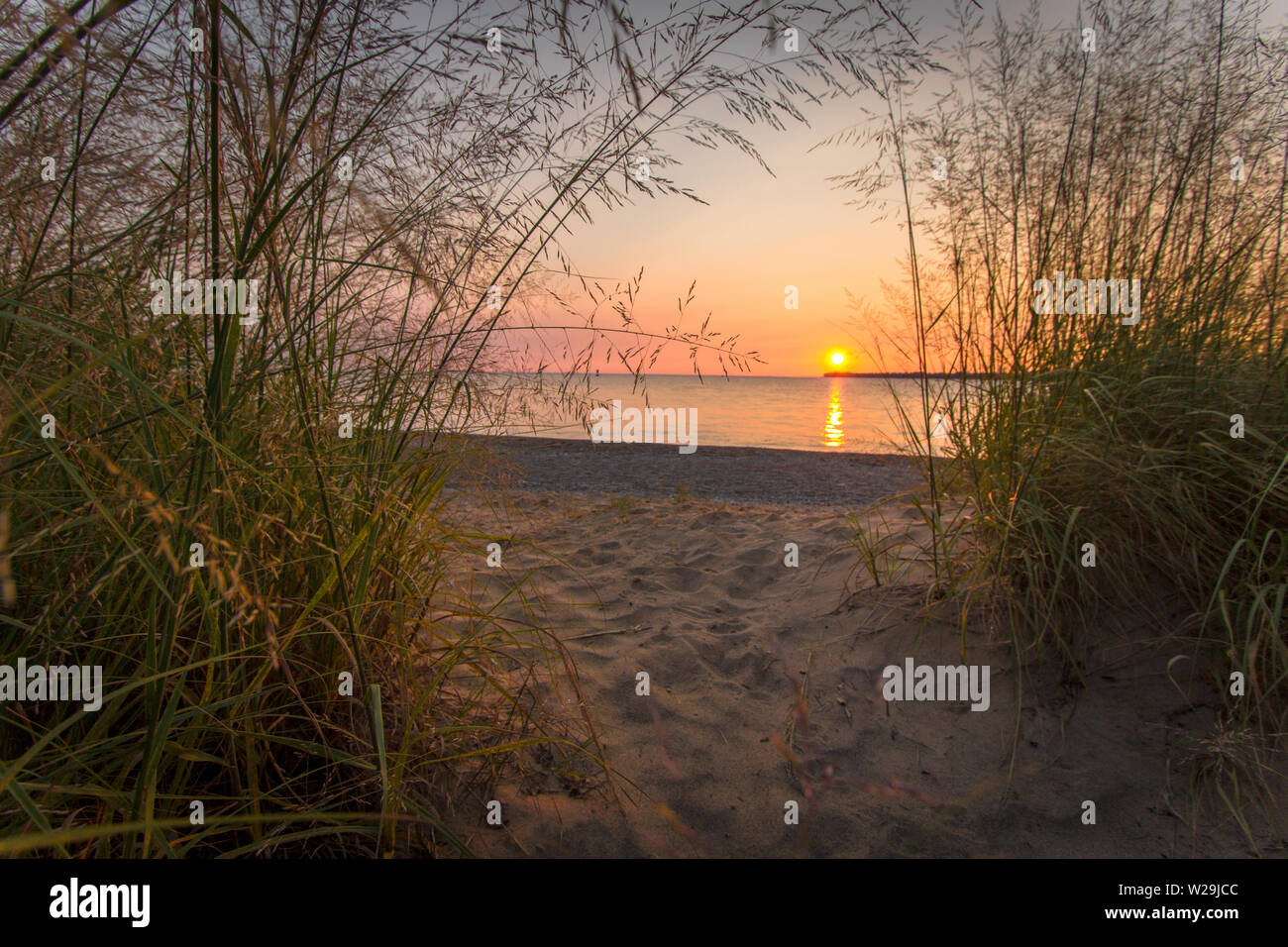 Sunset Trail. Sandy beach with trail through dune grass and setting sun over the water. Lighthouse Beach, Port Huron, Michigan. Stock Photo