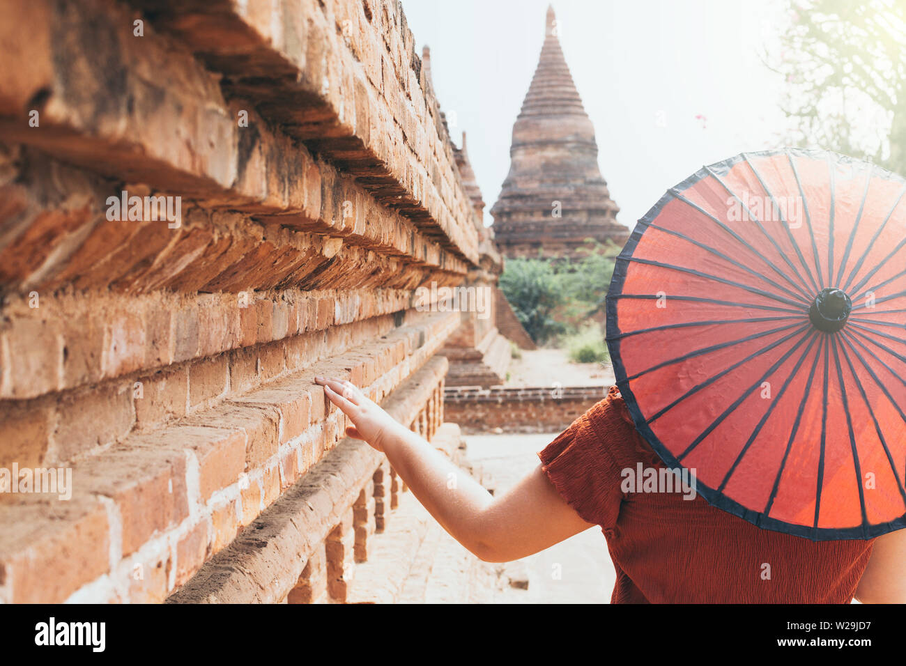 Woman with traditional Burmese red umbrella overlooking pagoda and temple of ancient Bagan in Myanmar Stock Photo