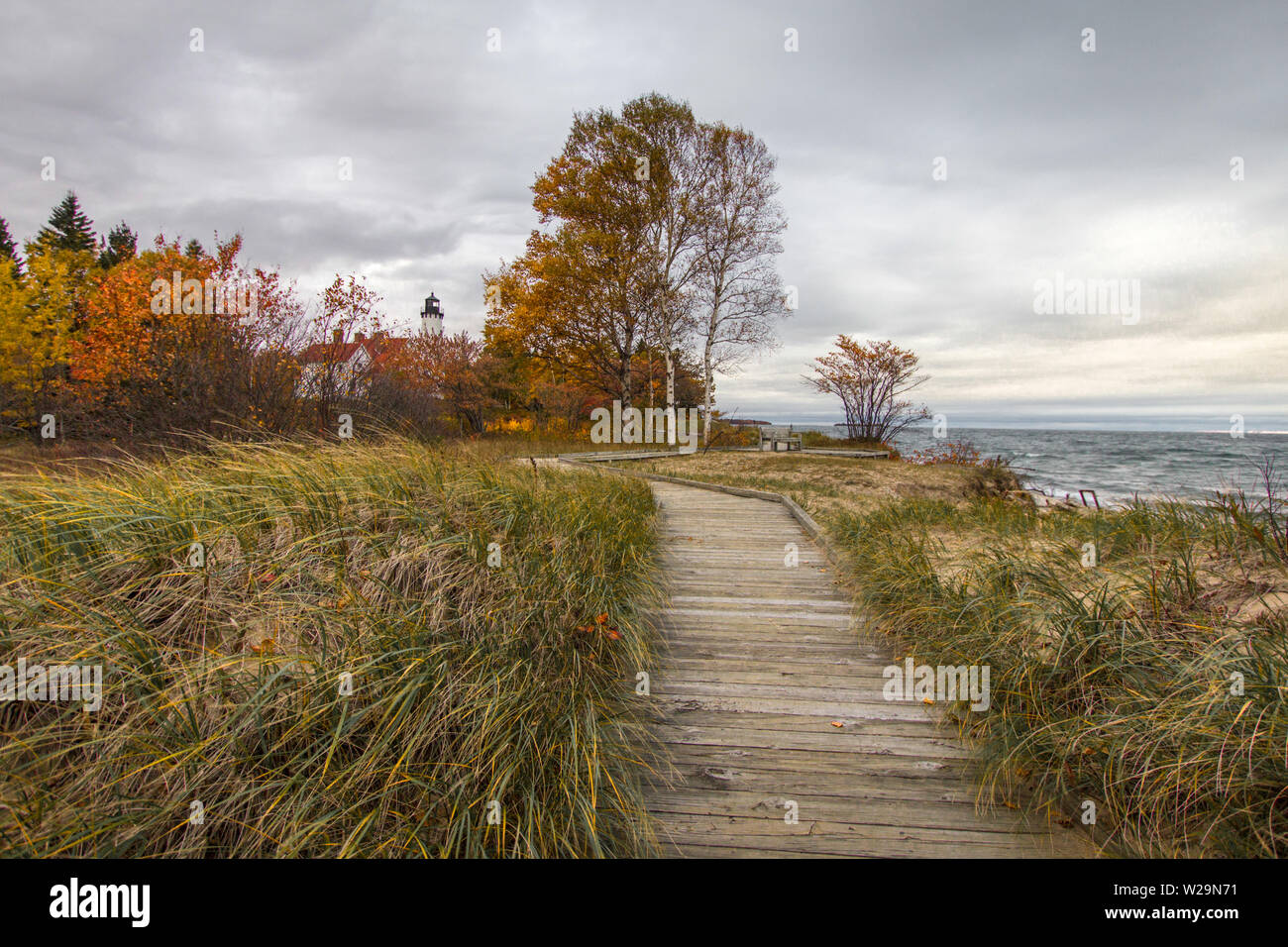 Boardwalk On Beach. Boardwalk trail through dune grass with the Point Iroquois lighthouse along Lake Superior in Hiawatha National Forest of Michigan. Stock Photo